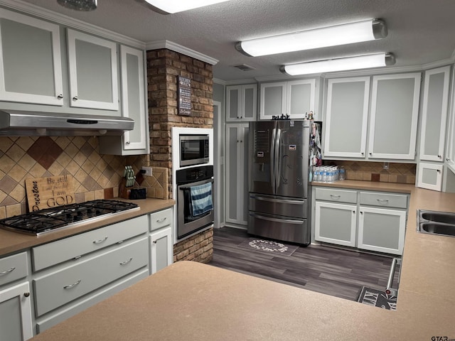 kitchen featuring decorative backsplash, dark wood-type flooring, ornamental molding, stainless steel appliances, and a textured ceiling