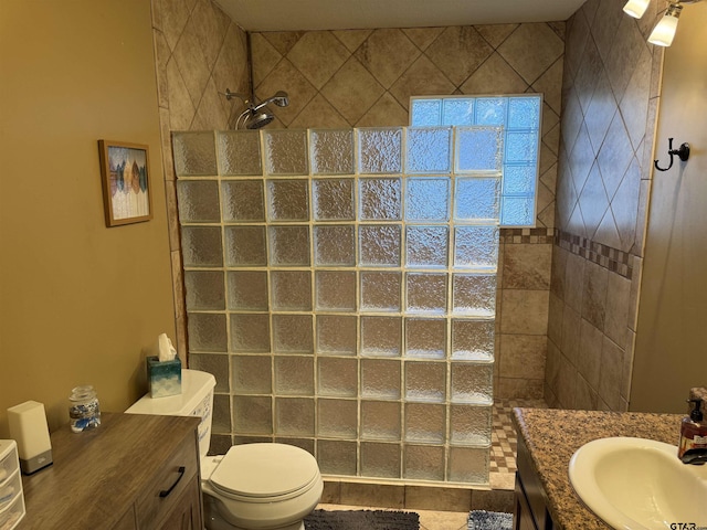 bathroom with toilet, a tile shower, tile patterned floors, and vanity