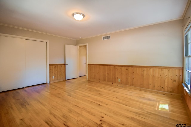 unfurnished room with crown molding, wooden walls, and light hardwood / wood-style floors