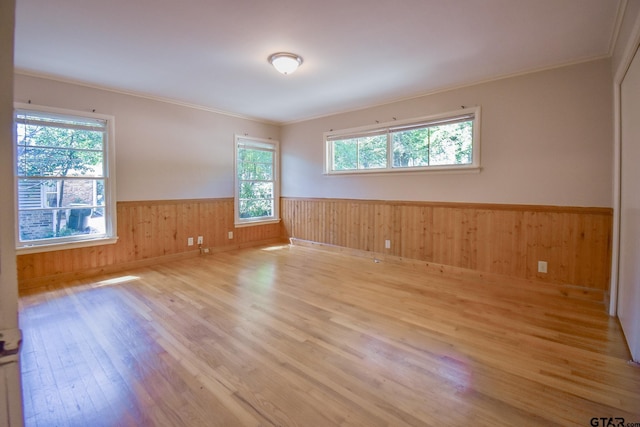 unfurnished room with ornamental molding, wooden walls, and light wood-type flooring