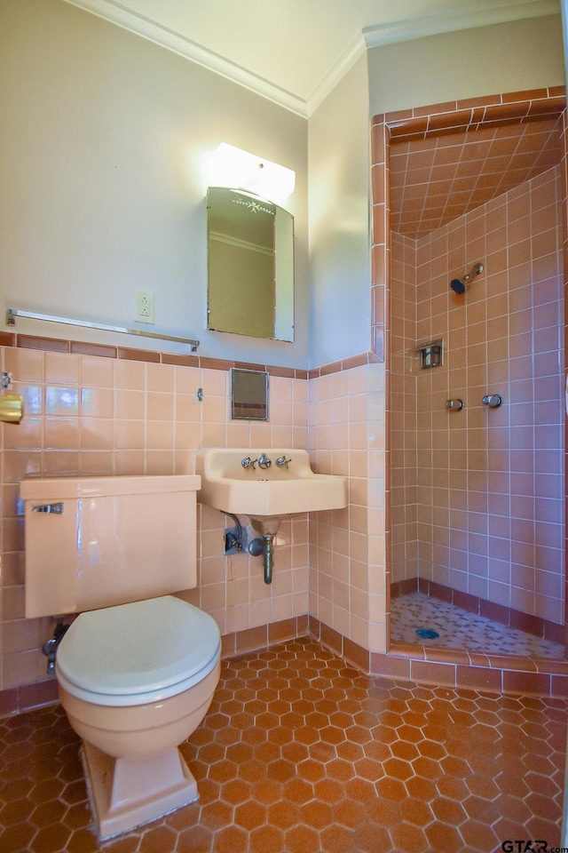 bathroom with tile walls, tiled shower, toilet, crown molding, and tile patterned floors