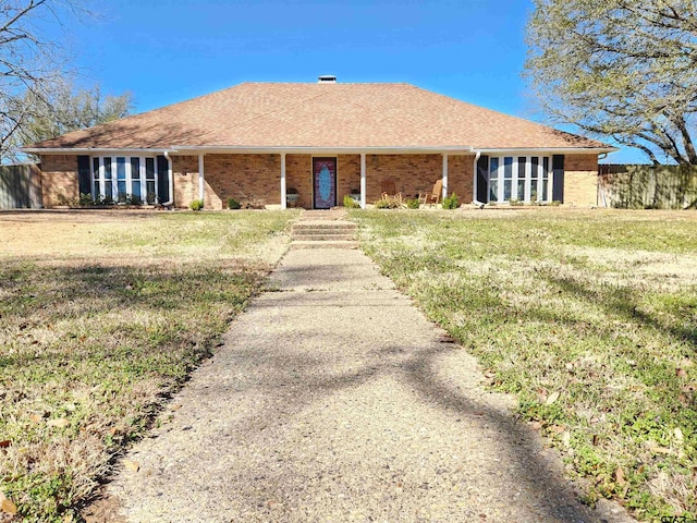 back of house featuring brick siding, roof with shingles, a lawn, and fence