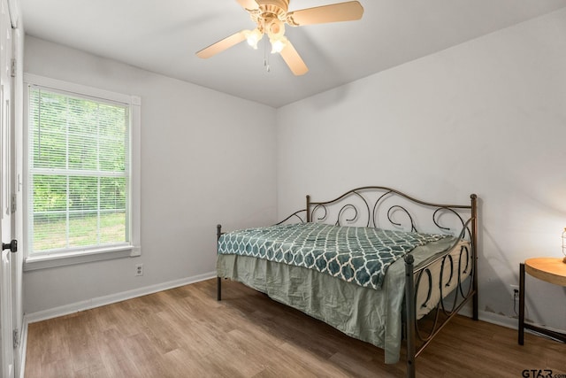 bedroom featuring baseboards, a ceiling fan, wood finished floors, and multiple windows