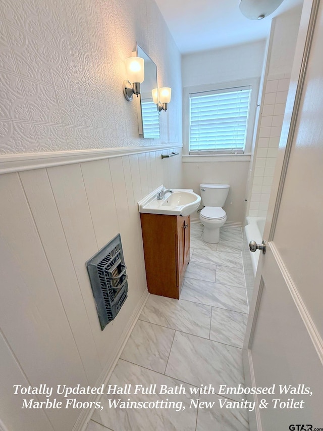 902 W 9th St, Tyler, TX 75701 - bathroom featuring vanity, marble look tile flooring, toilet, wainscoting, and a bathtub