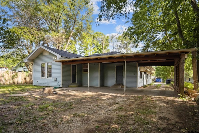back of property featuring fence, dirt driveway, and an attached carport