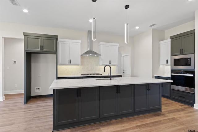 kitchen featuring light stone countertops, appliances with stainless steel finishes, sink, wall chimney range hood, and white cabinetry