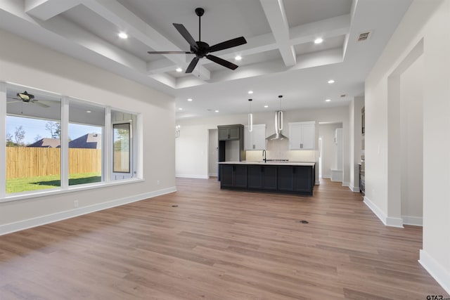 unfurnished living room featuring coffered ceiling, sink, hardwood / wood-style flooring, ceiling fan, and beamed ceiling