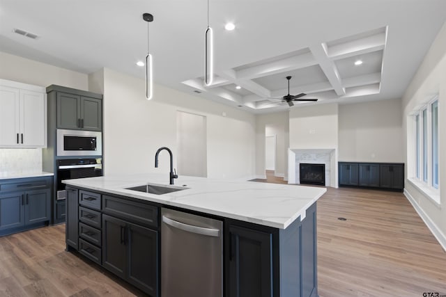 kitchen with sink, stainless steel appliances, coffered ceiling, light stone counters, and a kitchen island with sink