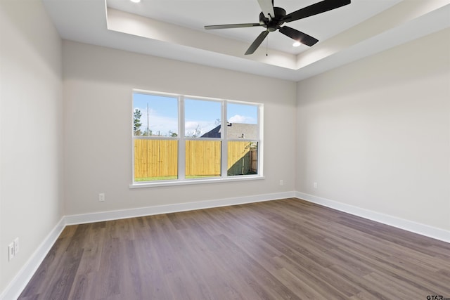 spare room with a tray ceiling, ceiling fan, and dark wood-type flooring