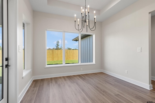 unfurnished dining area featuring a tray ceiling, a chandelier, and light hardwood / wood-style floors