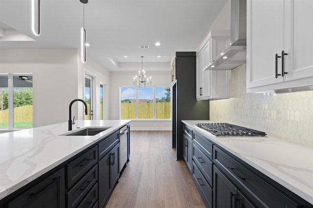 kitchen featuring sink, hanging light fixtures, wall chimney range hood, white cabinets, and plenty of natural light