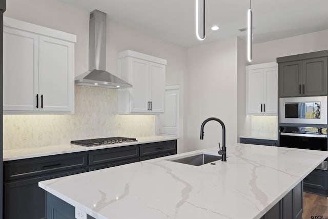 kitchen featuring appliances with stainless steel finishes, wall chimney range hood, sink, and a kitchen island with sink