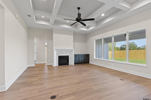 unfurnished living room featuring coffered ceiling, light hardwood / wood-style flooring, ceiling fan, a premium fireplace, and beam ceiling