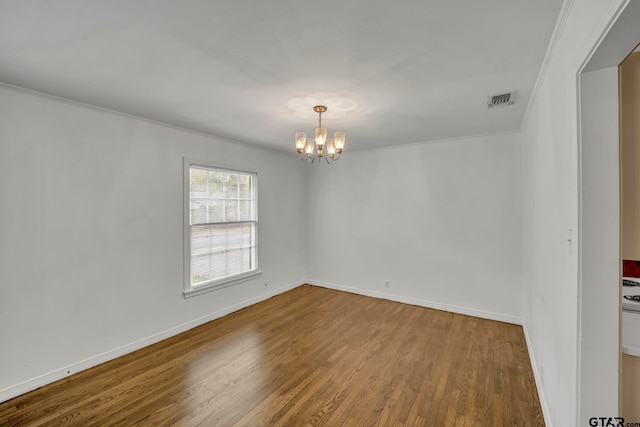 empty room with hardwood / wood-style floors, a notable chandelier, and ornamental molding