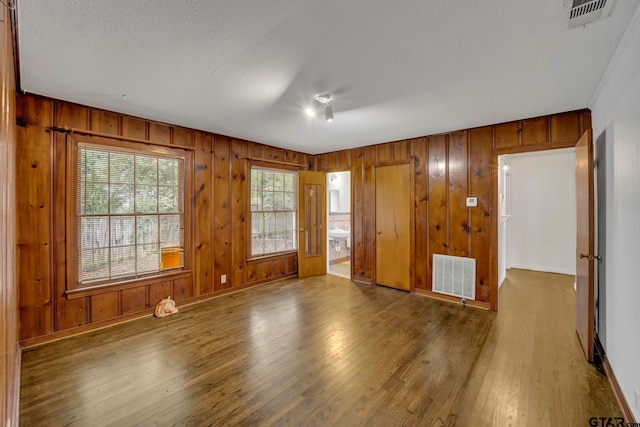 empty room with dark hardwood / wood-style floors, wooden walls, and a textured ceiling