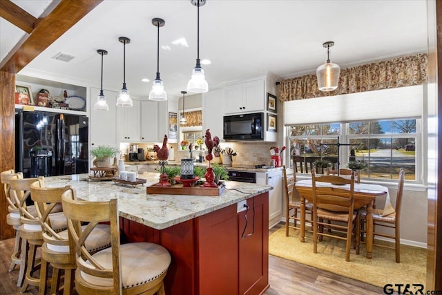 kitchen featuring a center island, decorative light fixtures, black appliances, light stone countertops, and white cabinets