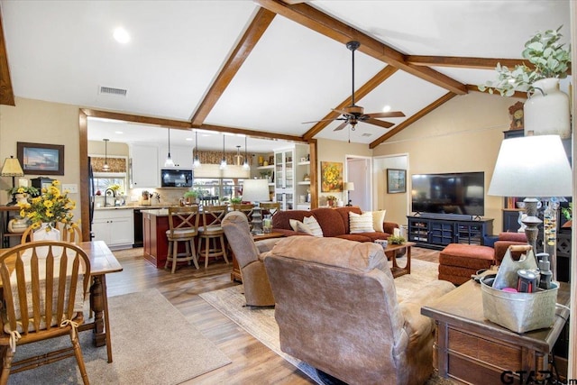 living room featuring light wood-type flooring, sink, lofted ceiling with beams, and ceiling fan