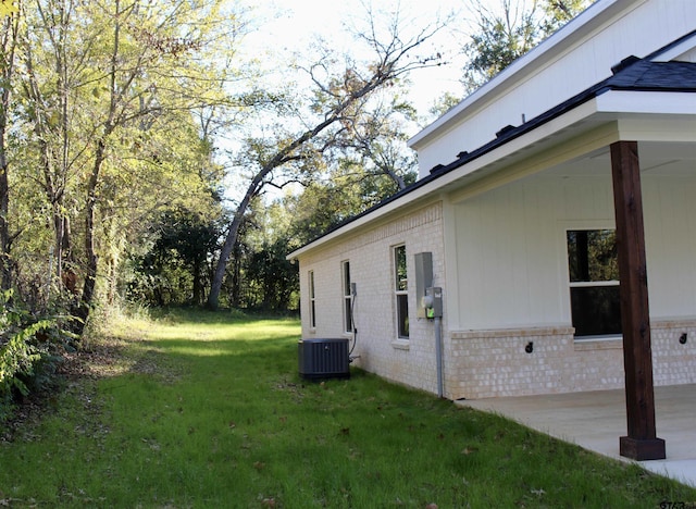 view of side of home featuring brick siding, a yard, central AC, and a patio