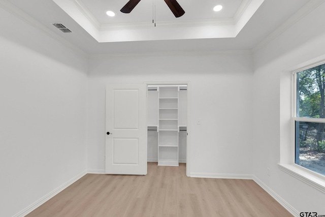 unfurnished bedroom featuring a tray ceiling, crown molding, visible vents, light wood-style floors, and baseboards