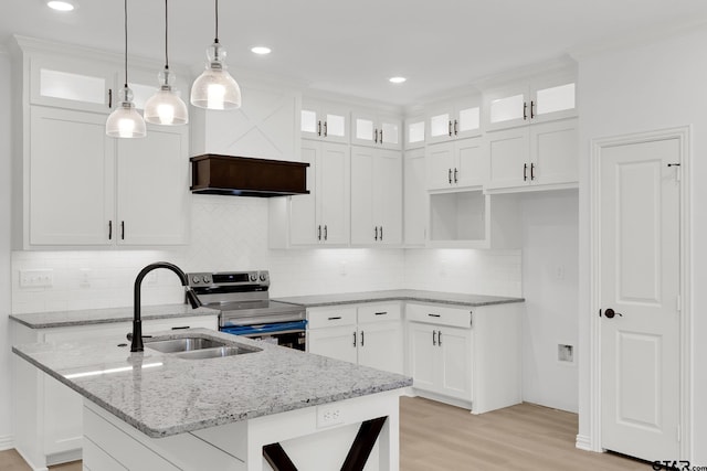 kitchen with glass insert cabinets, white cabinets, electric stove, a center island with sink, and pendant lighting