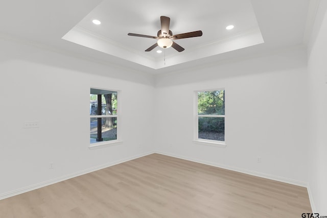 empty room with baseboards, a tray ceiling, light wood-style floors, and crown molding