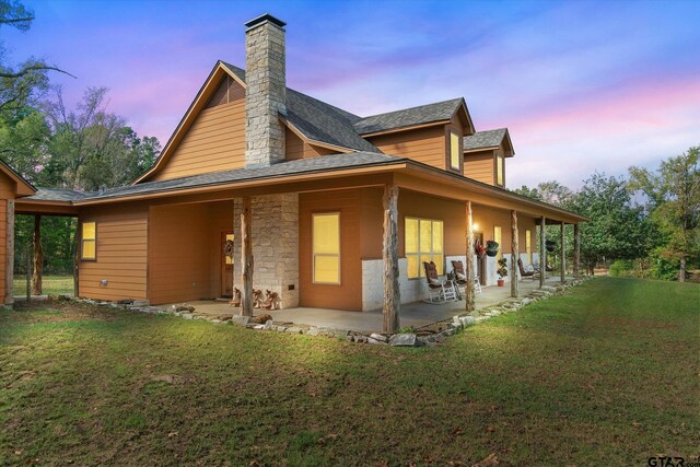 back house at dusk featuring a patio area and a lawn