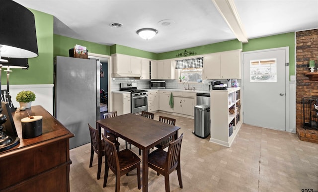 kitchen featuring stainless steel appliances, beamed ceiling, sink, backsplash, and white cabinets