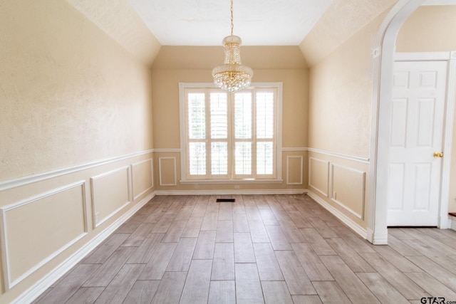 empty room with wood finish floors, arched walkways, a chandelier, and vaulted ceiling