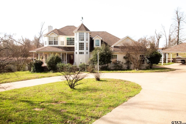 view of front of home with curved driveway, a chimney, and a front lawn