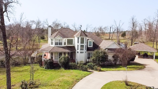 view of front facade with a front lawn, a porch, concrete driveway, a carport, and a chimney