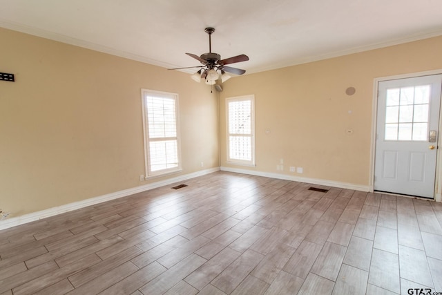 empty room with baseboards, visible vents, light wood finished floors, ceiling fan, and crown molding