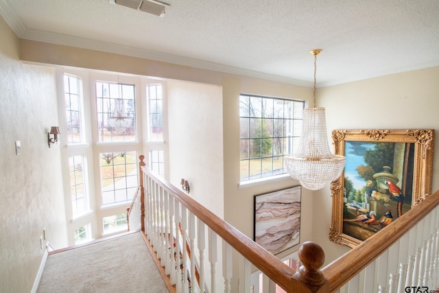 hallway featuring ornamental molding, a textured ceiling, carpet flooring, an upstairs landing, and a chandelier