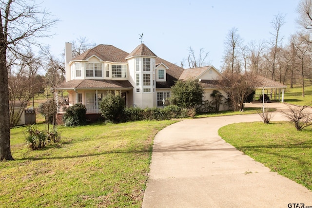 victorian home featuring covered porch, curved driveway, a chimney, and a front yard