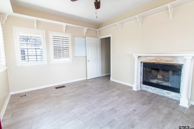 unfurnished living room with visible vents, baseboards, ceiling fan, a premium fireplace, and wood finished floors