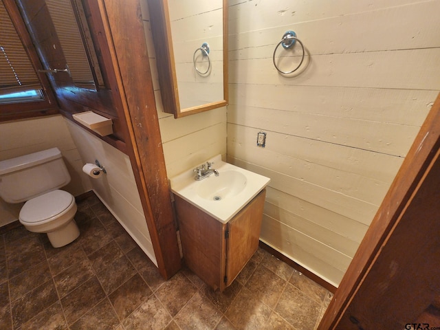 bathroom with vanity, toilet, and wood walls