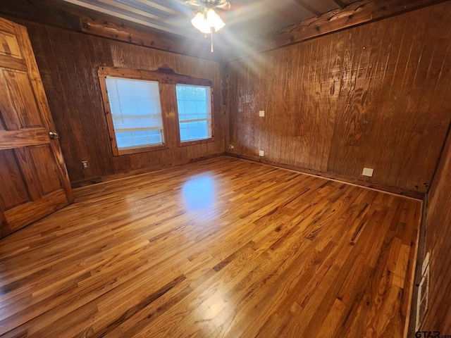 unfurnished room with hardwood / wood-style flooring, ceiling fan, and wood walls