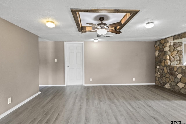 spare room featuring wood finished floors, a textured ceiling, ceiling fan, baseboards, and visible vents
