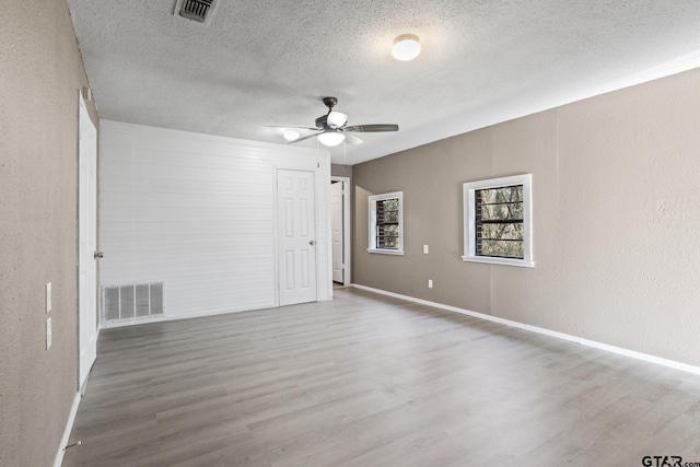 spare room featuring a textured ceiling, wood finished floors, visible vents, and a ceiling fan