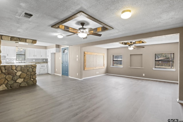unfurnished living room with wood finished floors, visible vents, a ceiling fan, a healthy amount of sunlight, and a textured ceiling