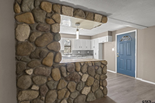 kitchen with a textured ceiling, backsplash, a peninsula, white cabinetry, and dark wood-type flooring