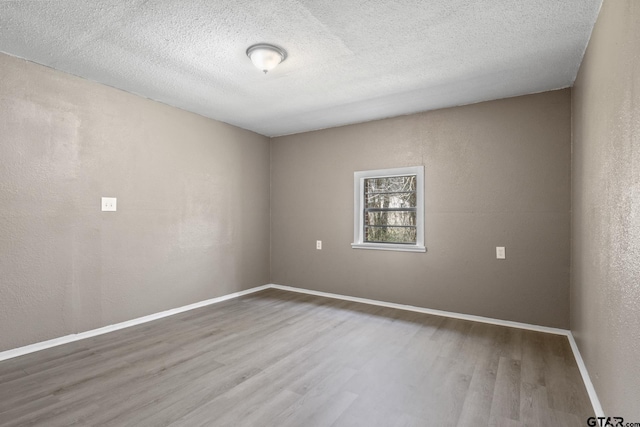 empty room with wood finished floors, a textured ceiling, and baseboards
