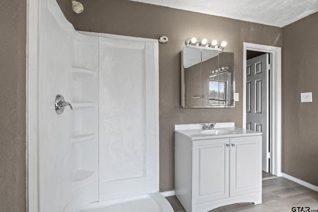 full bathroom with a textured wall, baseboards, walk in shower, and wood finished floors