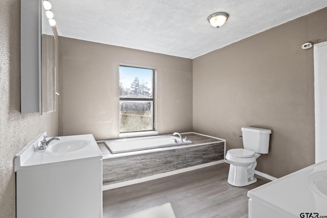 bathroom with a textured ceiling, toilet, wood finished floors, a garden tub, and vanity