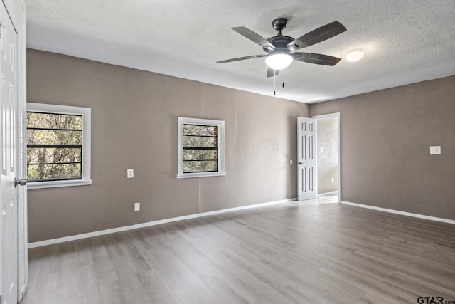 unfurnished room with ceiling fan, baseboards, wood finished floors, and a textured ceiling