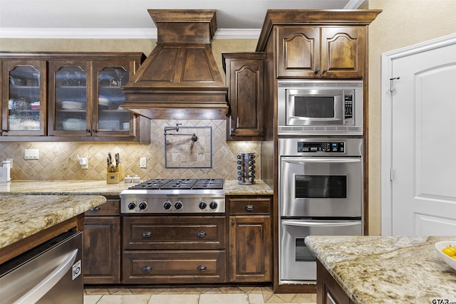 11187 Hunters Trl, Flint, TX 75762 - kitchen with appliances with stainless steel finishes, premium range hood, tasteful backsplash, dark brown cabinetry, and ornamental molding