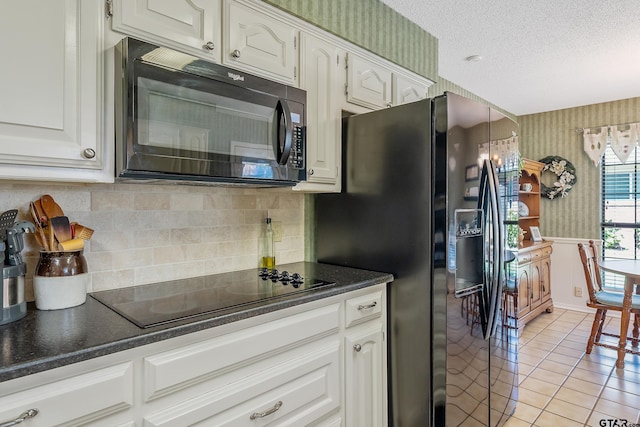 kitchen featuring light tile patterned flooring, white cabinets, black appliances, and a textured ceiling