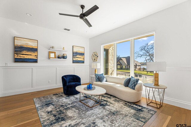 living area with hardwood / wood-style floors, a ceiling fan, a decorative wall, and visible vents