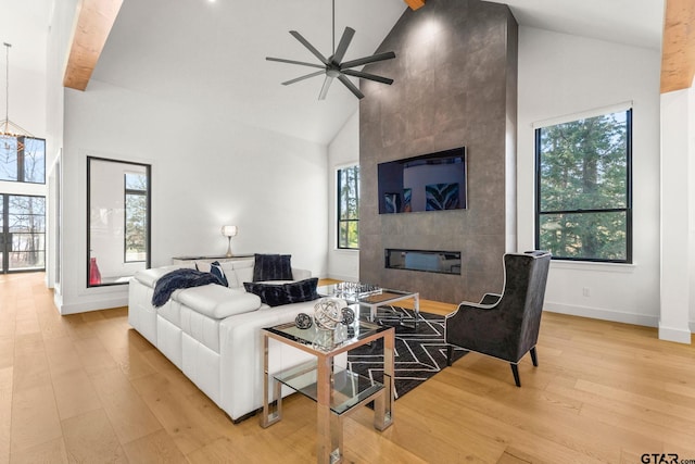 living room with high vaulted ceiling, a tile fireplace, baseboards, a ceiling fan, and light wood-style floors