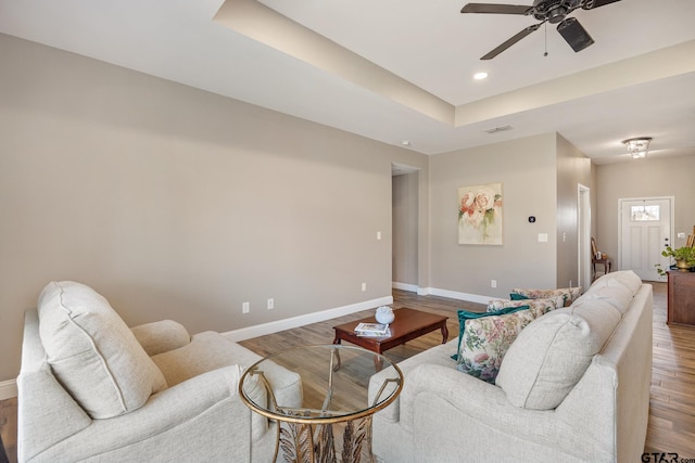 living room with a tray ceiling, wood-type flooring, and ceiling fan