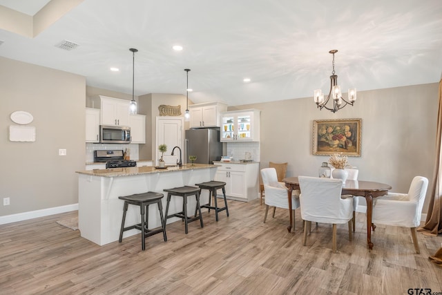 kitchen featuring white cabinetry, appliances with stainless steel finishes, light stone countertops, decorative light fixtures, and decorative backsplash